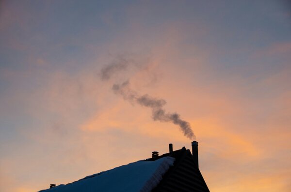 Rauch steigt aus einem Schornstein vor einem farbenfrohen Sonnenuntergang auf.